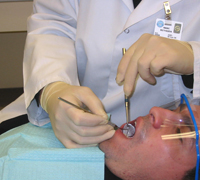 Christopher Beadle uses a dental mirror and scaler to clean a patient's teeth.