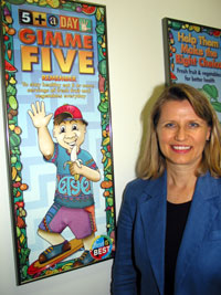 Gloria Stables stands next to a 5 A Day Program poster 